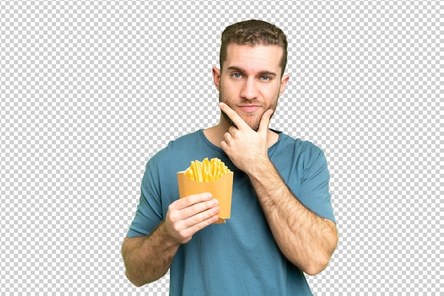 Jovem homem loiro bonito segurando batatas fritas sobre isolado pensamento de fundo chave de croma