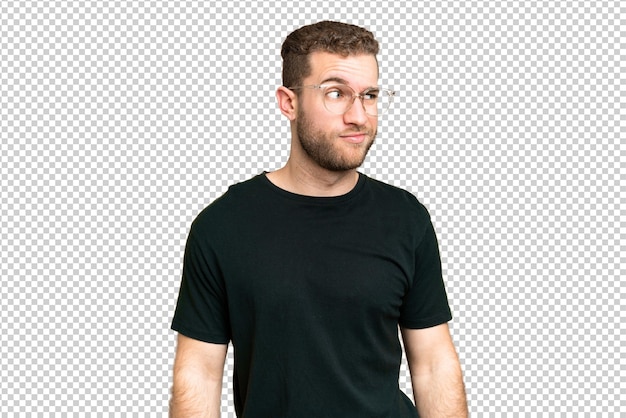 Jovem homem loiro bonito sobre isolado chroma chave fundo tendo dúvidas enquanto olhando para o lado