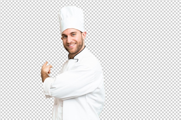Jovem homem loiro Chef sobre isolado chroma chave fundo apontando para trás
