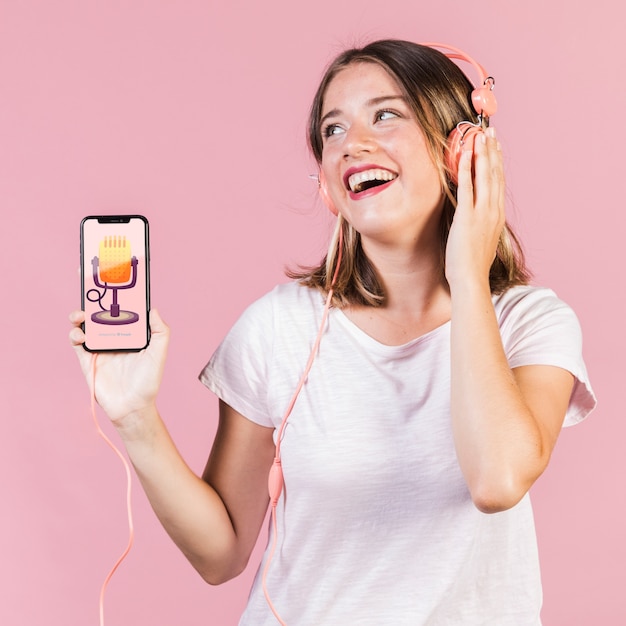 Jovem mulher com fones de ouvido, segurando um modelo de celular a rir