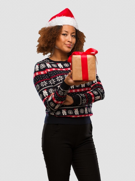 Jovem mulher negra segurando um presente no dia de natal, olhando para a frente