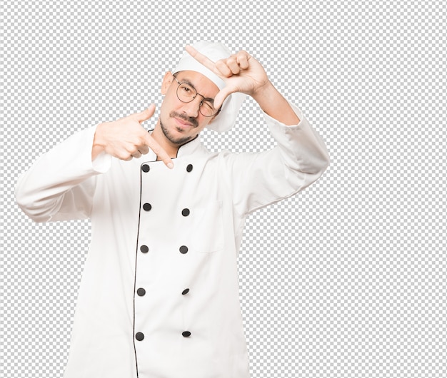 Joven chef sorprendido haciendo un gesto de tomar una foto con las manos