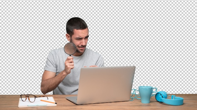 Joven concentrado usando una lupa en su computadora portátil