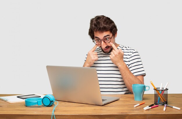 Joven diseñador gráfico barbudo con una computadora portátil mirando, observando, vigilando un objeto