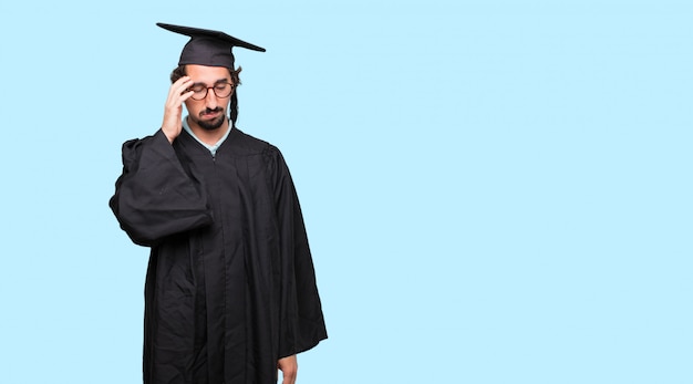 Joven graduado sonriendo y apuntando hacia arriba con ambas manos