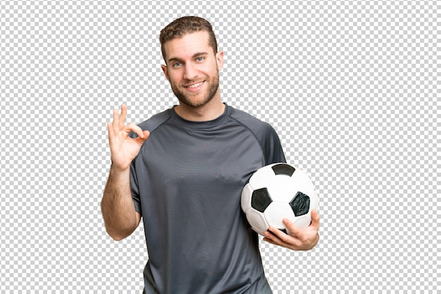 Joven hombre rubio guapo sobre fondo de llave cromada aislado con pelota de fútbol y haciendo el signo OK