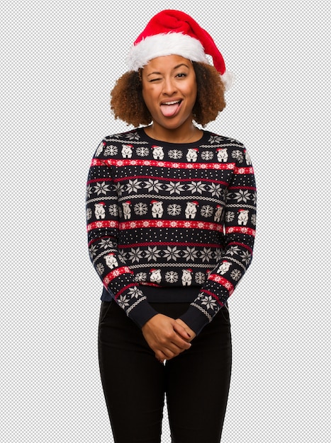 Joven mujer negra en un suéter navideño de moda con estampado divertido y amigable que muestra la lengua
