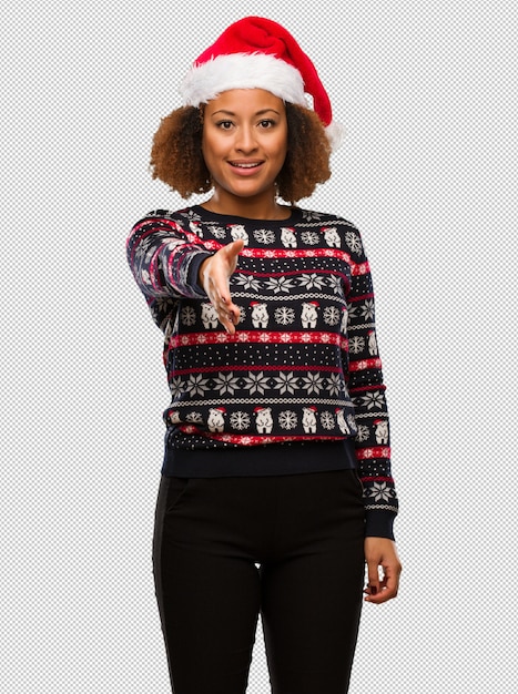 Joven mujer negra en un suéter navideño de moda con estampado que se extiende para saludar a alguien