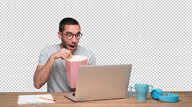 PSD joven sorprendido mirando una película en su computadora portátil y comiendo palomitas de maíz