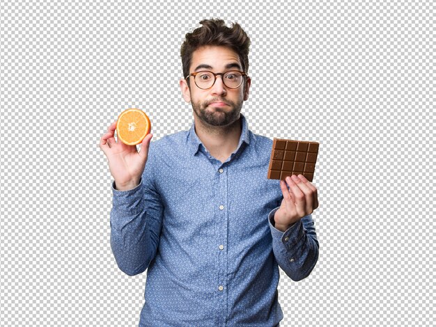 Joven sosteniendo una naranja y una barra de chocolate