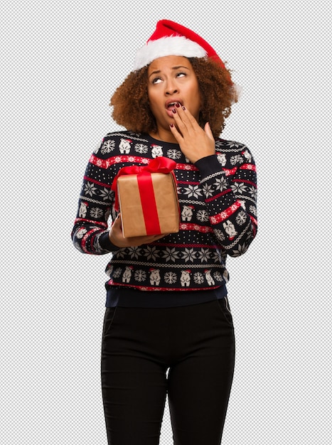 Junge schwarze frau, die ein geschenk am weihnachtstag müde und sehr schläfrig hält