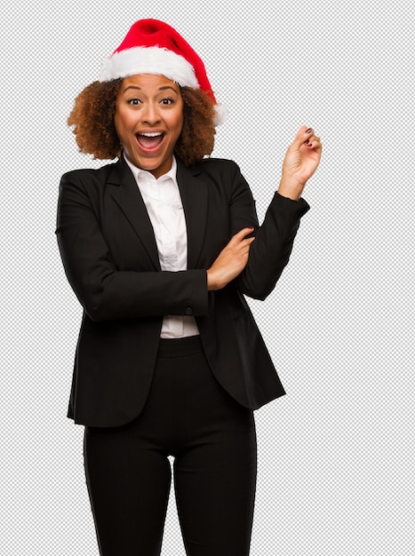 Junge schwarze Geschäftsfrau, die einen Weihnachtssankt-Hut zeigt auf die Seite mit dem Finger trägt