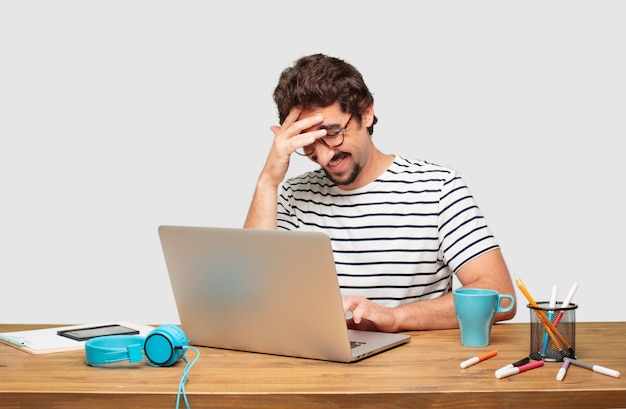 junger bärtiger Grafikdesigner mit einem Laptop, der glücklich einige gute und überraschende Nachrichten verwirklicht