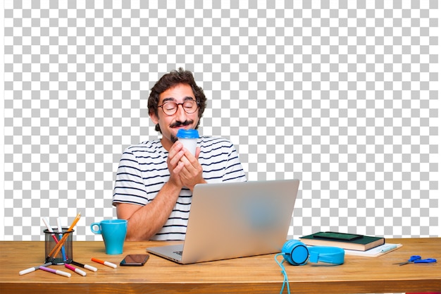Junger verrückter Grafikdesigner auf einem Schreibtisch mit einem Laptop und mit einem Kaffee zum Mitnehmen