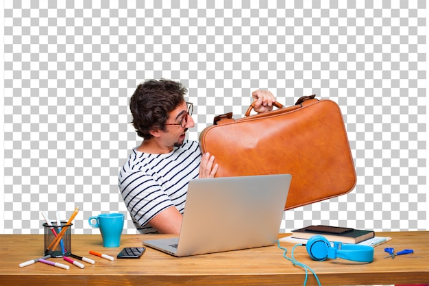 Junger verrückter grafikdesigner auf einem schreibtisch mit einem laptop und mit einem lederkoffergepäck