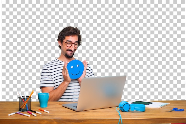 Junger verrückter grafikdesigner auf einem schreibtisch mit einem laptop und mit einem smiley emoticon