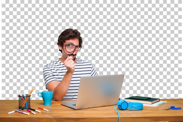 Junger verrückter grafikdesigner auf einem schreibtisch mit einem laptop und mit einer lupe