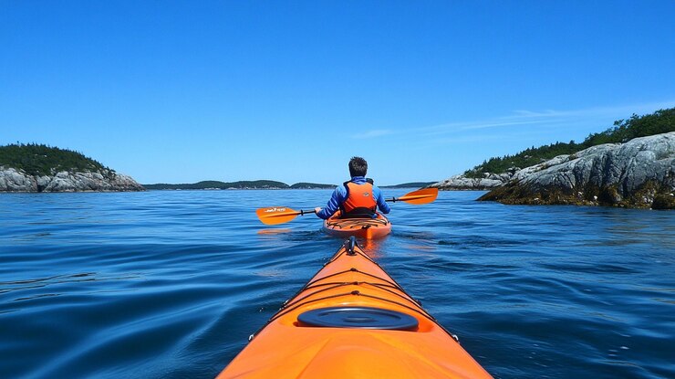 PSD kayaker remando en las aguas tranquilas del océano hacia islas rocosas bajo un cielo azul claro