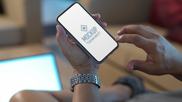 Kurzer Schuss von männlichen Händen, die auf verspottetem Smartphone berühren, während entspanntes Sitzen im Wohnzimmer