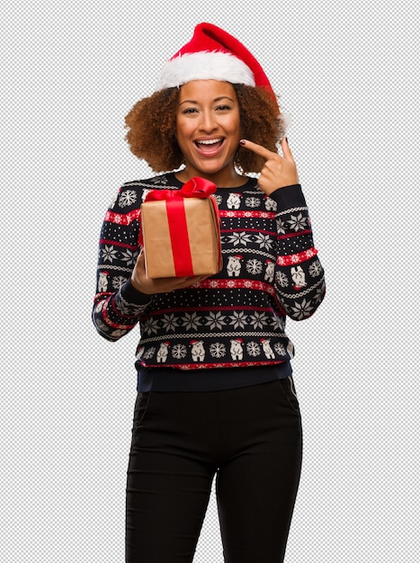 La giovane donna di colore che tiene un regalo nel giorno di Natale sorride, indicando la bocca
