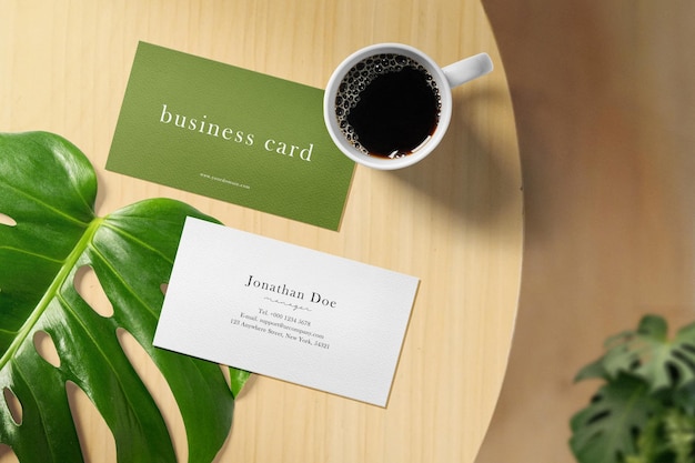 Limpe a maquete mínima do cartão de visita no fundo da mesa com folhas de plantas e café