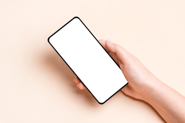 Main féminine tenant un téléphone avec un écran vide sur un fond beige