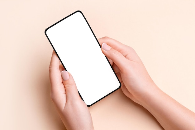 Main féminine tenant un téléphone avec un écran vide sur un fond beige