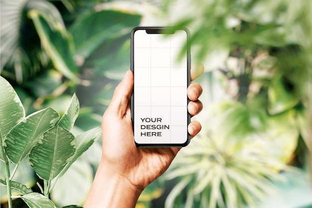 Main tenant une nouvelle maquette de smartphone entourée de feuilles