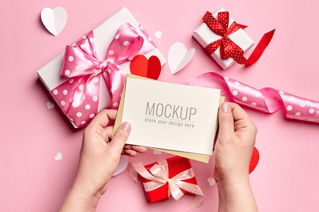 Mani che tengono il mockup di carta di San Valentino con scatole regalo e cuori di carta