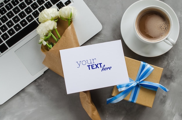 Manichino di biglietto di auguri con computer portatile, confezione regalo, caffè del mattino e fiori.
