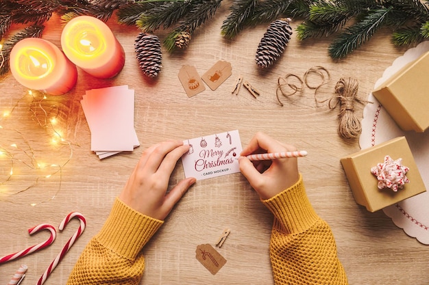 Mano di donna che scrive un modello di biglietto di auguri di Natale su un tavolo di legno con roba di Natale in posizione piatta