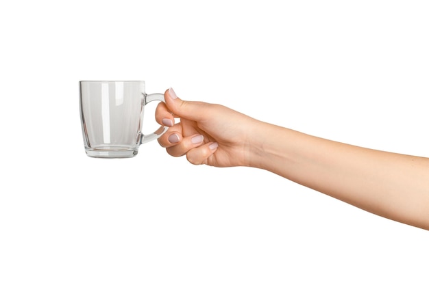mano femenina sosteniendo una taza de vidrio vacía en un fondo vacío.