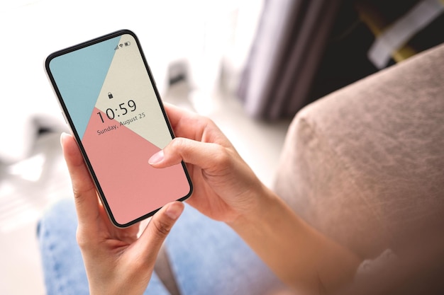 Mano de mujer de maqueta sosteniendo el teléfono inteligente negro con pantalla en blanco en el sofá en casa. Concepto de negocio y tecnología