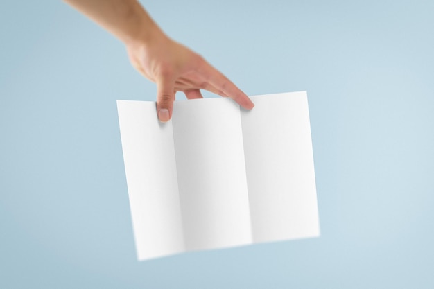 La mano sostiene un folleto blanco triplo contra un fondo azul