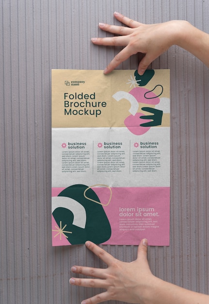 Manos femeninas sosteniendo maqueta de folleto tríptico con formas abstractas