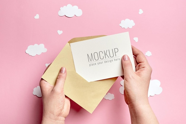 Manos sosteniendo maqueta de tarjeta de felicitación con nubes de papel y corazones en rosa
