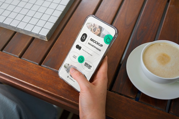 Mão de alto ângulo com smartphone e café