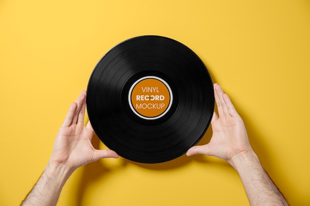 Mãos segurando um disco de vinil com fundo amarelo