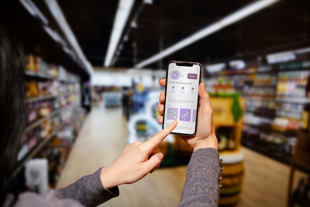 PSD mãos segurando um smartphone no supermercado