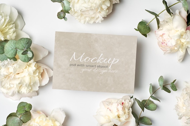 Maqueta estacionaria de invitación o tarjeta de felicitación con flores de peonía blanca y ramitas de eucalipto