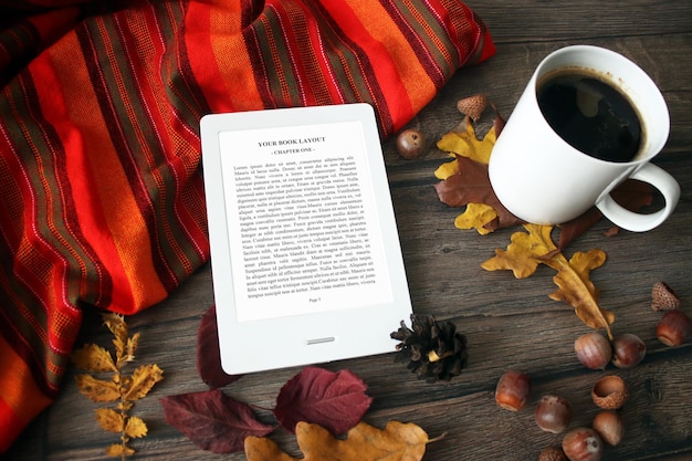 Maqueta de lector de libros electrónicos con hojas de otoño, cono de pino, café, castañas y manta, cálido, acogedor, colo