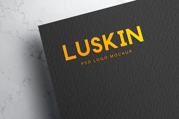 maqueta de logotipo dorado en relieve sobre papel negro blanco