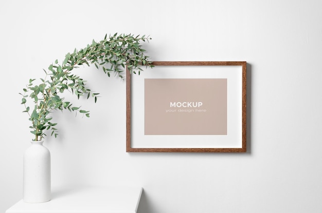 PSD maqueta de marco de madera de paisaje en pared blanca con planta verde