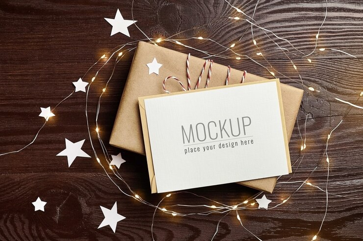Maqueta de tarjeta de felicitación con caja de regalo y luces navideñas en mesa de madera