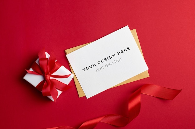 Maqueta de tarjeta de felicitación con caja de regalo sobre fondo rojo