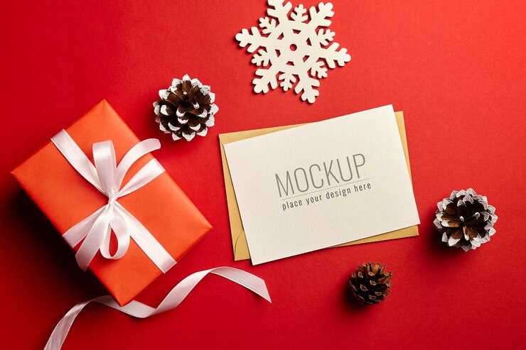 Maqueta de tarjeta de felicitación de Navidad con caja de regalo y adornos sobre fondo rojo.