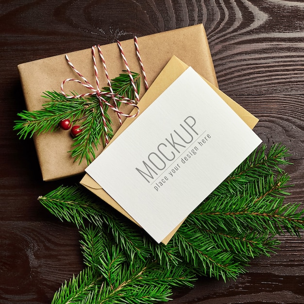 Maqueta de tarjeta de felicitación de navidad con caja de regalo y ramas de abeto sobre fondo de madera