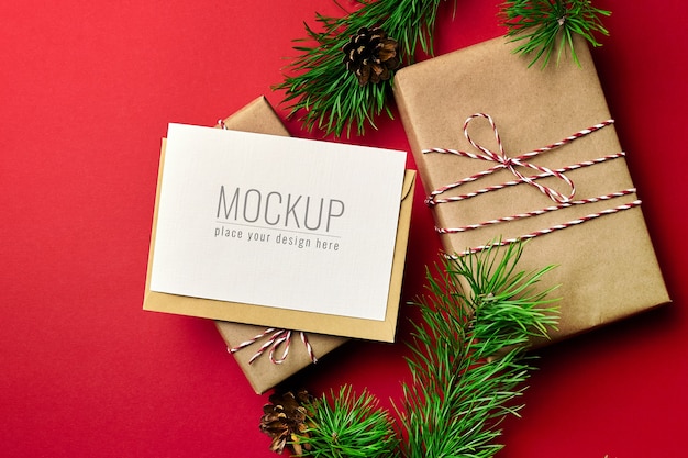 Maqueta de tarjeta de felicitación de Navidad con cajas de regalo y ramas de pino sobre fondo rojo.