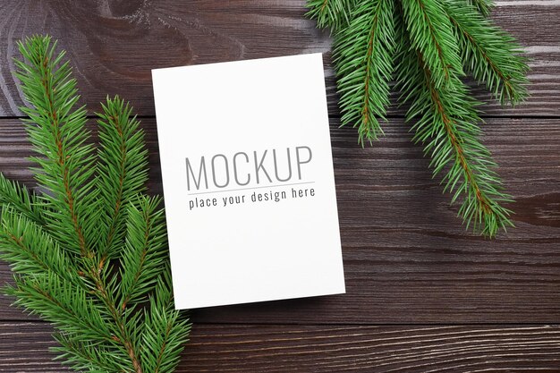 PSD maqueta de tarjeta de felicitación de navidad con ramas de abeto verde sobre fondo de madera oscura.