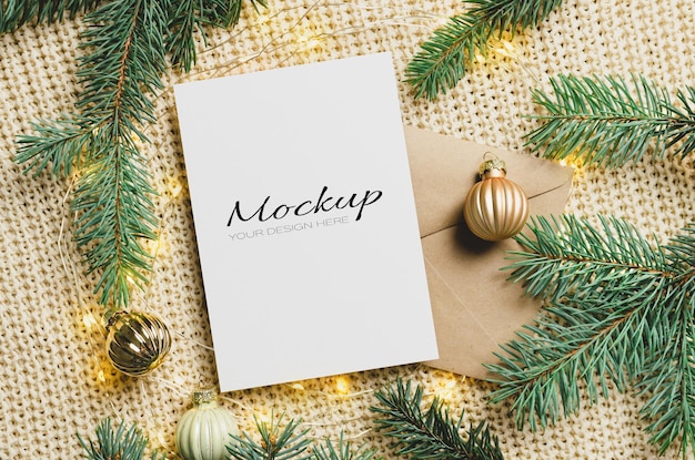 Maqueta de tarjeta de felicitación navideña con sobre, decoraciones festivas y ramas de abeto con luces